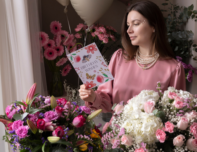Woman holding a birthday wishes card surrounded by pink and white flower bouquets from Flowers.ie